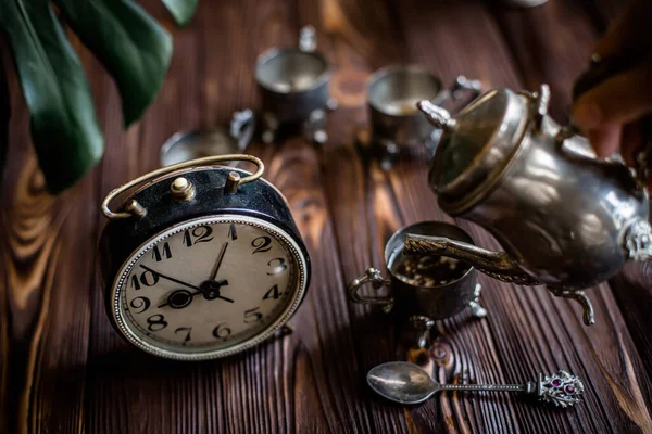 Kahvaltıda. Eski bir kahve demliğinden el yapımı kahve. Eski bir çalar saatin yanında gümüş bir kupa.