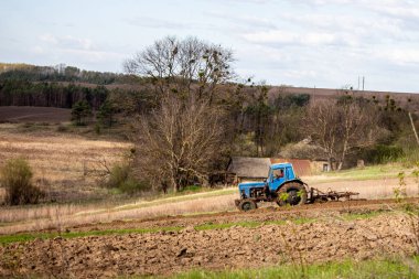 Tarlada sabanı olan eski mavi traktör ve Ukrayna köyündeki tepelik arazinin arka planında toprak yetiştiriyor. Baharda toprağı sebze ekmeye hazırlıyorum. Tarım makineleri, saha çalışması