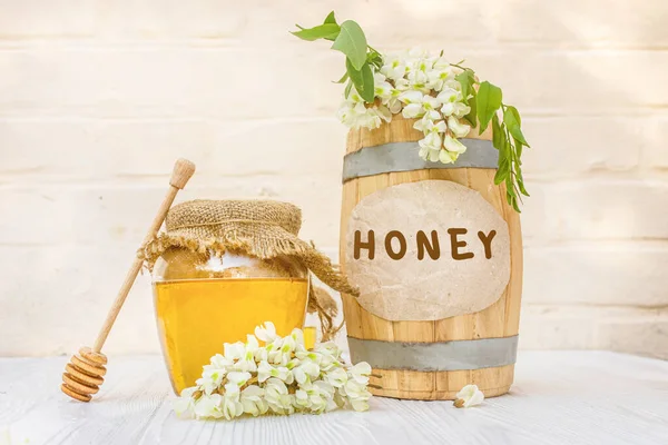新鮮な液体アカシア蜂蜜の収穫2021木製の樽と蓋にキャンバスナプキンと透明な瓶で 花の枝白いアカシア 蜂蜜のための霧雨の横にあるロビン — ストック写真