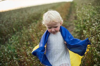 Ukrayna bayrağı gülümseyen küçük kızın ellerinde. Mutlu çocuk sarı-mavi bayrak taşıyor. Ukrayna 'nın güvensizliği günü. Bayrağa seçici odaklanma