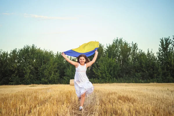 Laughing girl with the flag of Ukraine runs on field of wheat. Fourth of July. Freedom. Independence Day. Patriotic holiday. Flag Day. Constitution day. Copy space