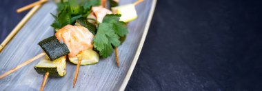 Gri tabakta yemeye hazır somon ve kabak kebabı..