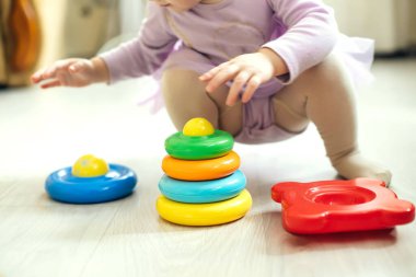 Kız güneşli bir günde oturma odasında yerde mantıksal piramit oynuyor. Montessori tahta oyuncağı katlanmış piramit. Çember, dörtgen, üçgen, çocuk oyuncaklarının tahta unsurlarını dikdörtgen yap. Çok renkli oyuncak mavi, sarı, kırmızı, yeşil
