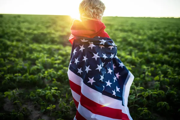 flag of America on shoulders of a child. girl in the background of sunset. Little American celebrates U.S. Independence Day on July 4.