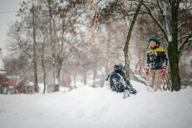 İki çocuk şehirde yoğun kar yağışı sonrasında kar yığınında oynuyorlar. Kışın parkta yürüyüş yapan çocuklar. Aktif sağlıklı yaşam tarzı.