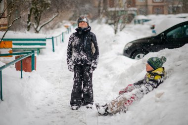 Kar dağında kızaklı, kayak kıyafeti giymiş bir çocuk. Çocuk bir kızak scooterına biniyor. Sokakta aktif oyunlar. Kış günü sağlıklı bir yaşam tarzı.
