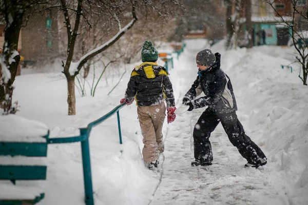 A boy in a ski suit on a snow mountain with a sled. The child is riding a sledge scooter . Active games on the street. Healthy lifestyle on winter day