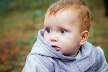 Scared baby looks aside. A small child looks puzzled. A girl in a purple jumpsuit in nature.