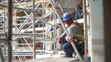 İnşaat işçisi iskele üzerinde diz çöküp çalışmaya hazırlanıyor..