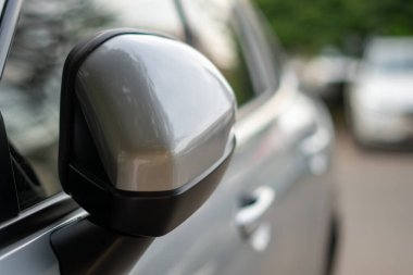 Close-up of a silver car side mirror with shallow depth of field and blurred outdoor background.