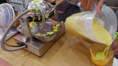The process of making waffles at an ice cream shop. Yellow batter is poured into hot, round metal molds, creating a lively and appetizing kitchen atmosphere with a distinctive sweet aroma.