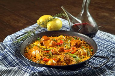 Valensiyalı Paella, klasik bir İspanyol yemeği, ahşap bir masada bir porron şarapla servis edilir.