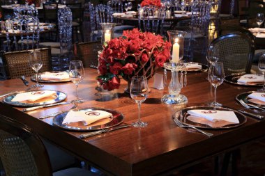 details of an exuberant and luxurious wedding party in a large hall, with candles, flowers and tables decorated in shades of red.