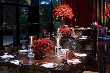 details of an exuberant and luxurious wedding party in a large hall, with candles, flowers and tables decorated in shades of red.