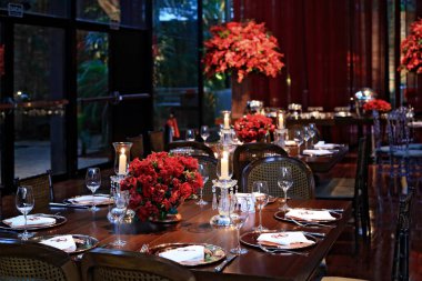 details of an exuberant and luxurious wedding party in a large hall, with candles, flowers and tables decorated in shades of red.