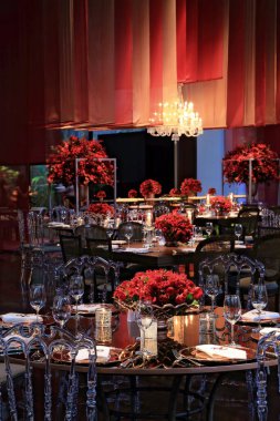 details of an exuberant and luxurious wedding party in a large hall, with candles, flowers and tables decorated in shades of red.