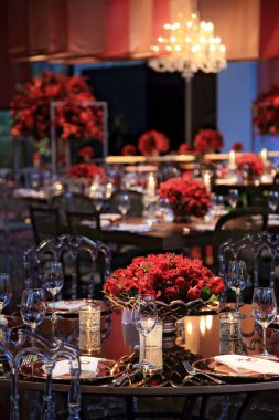 details of an exuberant and luxurious wedding party in a large hall, with candles, flowers and tables decorated in shades of red.