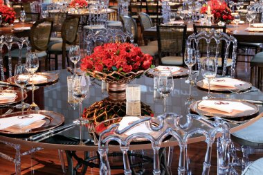 details of an exuberant and luxurious wedding party in a large hall, with candles, flowers and tables decorated in shades of red.