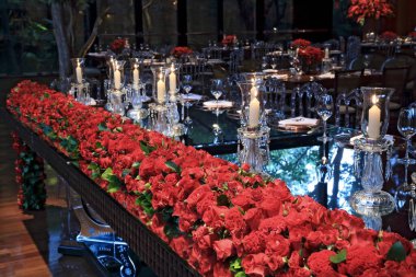 details of an exuberant and luxurious wedding party in a large hall, with candles, flowers and tables decorated in shades of red.