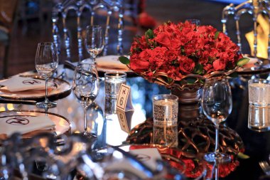 details of an exuberant and luxurious wedding party in a large hall, with candles, flowers and tables decorated in shades of red.
