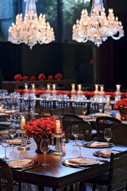 details of an exuberant and luxurious wedding party in a large hall, with candles, flowers and tables decorated in shades of red.