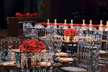 details of an exuberant and luxurious wedding party in a large hall, with candles, flowers and tables decorated in shades of red.