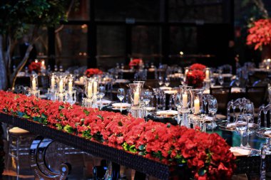 details of an exuberant and luxurious wedding party in a large hall, with candles, flowers and tables decorated in shades of red.