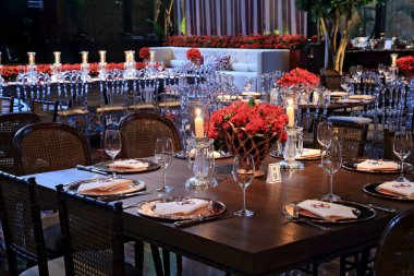 details of an exuberant and luxurious wedding party in a large hall, with candles, flowers and tables decorated in shades of red.