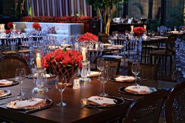 details of an exuberant and luxurious wedding party in a large hall, with candles, flowers and tables decorated in shades of red.