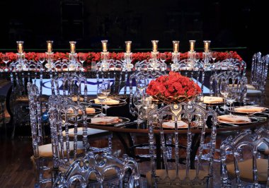details of an exuberant and luxurious wedding party in a large hall, with candles, flowers and tables decorated in shades of red.