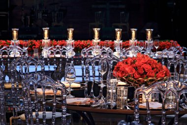 details of an exuberant and luxurious wedding party in a large hall, with candles, flowers and tables decorated in shades of red.