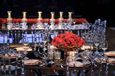 details of an exuberant and luxurious wedding party in a large hall, with candles, flowers and tables decorated in shades of red.