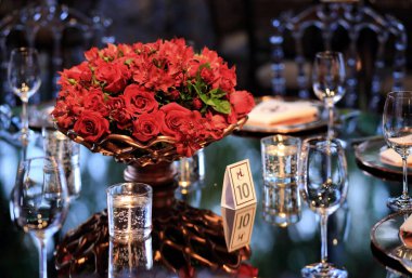 details of an exuberant and luxurious wedding party in a large hall, with candles, flowers and tables decorated in shades of red.