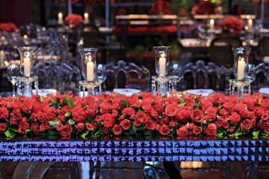 details of an exuberant and luxurious wedding party in a large hall, with candles, flowers and tables decorated in shades of red.