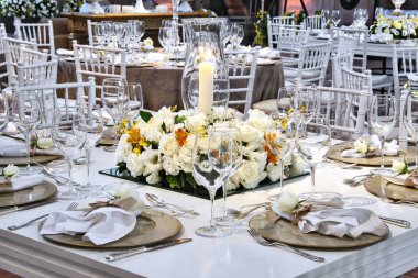 Altın tonlarda mumlar, çiçekler ve masalarla süslenmiş büyük bir salonda coşkulu ve lüks bir düğün partisinin ayrıntıları.