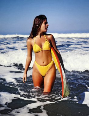 Sarı bikinili, sörf tahtası olan güzel sarışın manken denize giriyor..