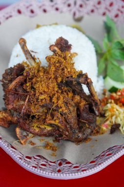 Kaldırım stili Madurese usulü kızarmış ördek. Kokulu baharatlar, beyaz pirinç, taze otlar, salatalık dilimleri ve hafif mango sambal ile servis ediliyor. Gıda görselleri için uygun, keskin bir aksan için.