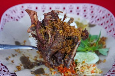 Kaldırım stili Madurese usulü kızarmış ördek. Kokulu baharatlar, beyaz pirinç, taze otlar, salatalık dilimleri ve hafif mango sambal ile servis ediliyor. Gıda görselleri için uygun, keskin bir aksan için.