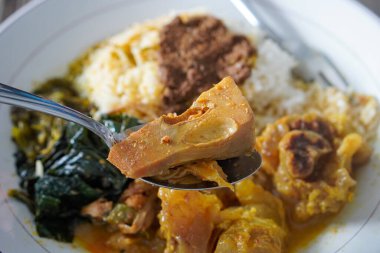 Padang bifteği tendon köri, sıcak pirinç, zengin hindistan cevizi sosu, taze tunjang parçaları, ve kalın Minang baharatları ile servis edilir doyurucu, lezzetli Endonezya yemeği atmosferi yaratır.