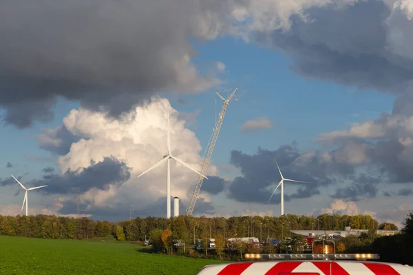 flashing lights of a working car and installation of new wind turbines and a beautiful cloudy sky in the background