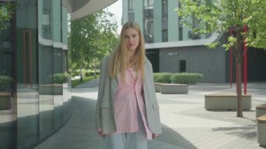 Sarışın Kadın Şehir Çevresindeki Kamerayla Yüzleşirken Tutkuyla Tartışıyor. Modern şehir manzarasında açık havada dururken el hareketleriyle hayal kırıklığını ifade eden kendinden emin bir kadın.