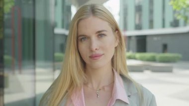 Çekici kadın saçını düzeltiyor ve dışarıdaki kameraya özgüvenle gülümsüyor. Zarif Kadın Modeli Kendine güvenen Saçlara Dokunuyor, Göz teması kuruyor ve Parlak Şehir Merkezinde Ilık Enerji Yayıyor