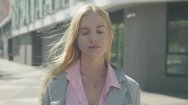 Huzurlu kadın gözlerini kapadı ve kameraya gülümsedi. Serene Outdoor Sahnesi Huzuru Yakalıyor, Kendine güven ve Parlak Şehir Merkezinde Pozitif Duygu. Yüksek kalite 4k görüntü