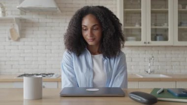 Afrikalı Kadın Parlak Ev Mutfağı 'nda dizüstü bilgisayar açarak Uzak İş Gününe Başlıyor. Sabah rutini, Üretken Atmosfer, Doğal Işıklı Modern Çalışma Alanı, Sakin Odaklı Ruh hali. Yüksek kalite 4k görüntü