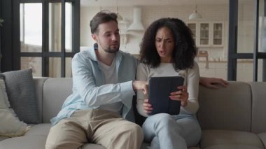 Çift, rahat koltukta tableti incelerken ev seçimlerini tartışıyor. Genç adam ve kadın, parlak oturma odasında yan yana oturuyor ve ev için iç tasarım kararı veriyorlar. Yüksek kalite 4k görüntü