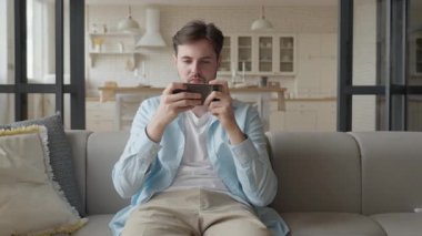 Adam evdeki rahat koltukta otururken mobil oyun kaybına tepki veriyor. Gerçek Hayat Duyguları ve Rahatlamış Ev Ayarları. Yüksek kalite 4k görüntü
