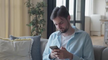 Akıllı Telefon Ekranı 'na Bakarken Heyecanlı Adam Başarı Kutlaması. Mutlu erkek, modern oturma odasında rahat bir koltukta otururken olumlu haberleri ya da kazanmayı sever. Yüksek kalite 4k görüntü