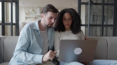 Cozy Modern Apartman 'daki dizüstü bilgisayarda internetten göz gezdirme seçenekleri. Rahatlamış Çiftler Dijital İçeriği Yanyana Keşfediyor Konforlu Oturma Odası kanepesinde, Karar Verme ya da Alışveriş Yapmaya Çalışıyor