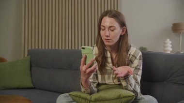 Oturma odasında tuhaf bir ifadeyle telefonda konuşan bir kadın. Dost canlısı bir kadın evdeki koltukta otururken sohbete daldı, özgün bir ilgi ve içsel duygu sergiliyor.