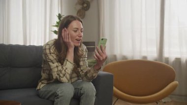 Oturma odasındaki telefon görüşmesinde şaşırmış kadının tepkisi. Olumlu Kadın Duygusu Parlak Modern Uzayda Yakalandı, İletişim, Yaşam Tarzı, Uzaktan Etkileşim, Teknoloji İçin Mükemmel